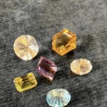 Assorted colorful gemstones in round, rectangular, and hexagonal shapes arranged on a dark textured surface by Creative Craftworks