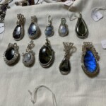 Colorful wire-wrapped gemstone pendants on white cloth, each with a price tag, showcasing a variety of colors and patterns at Creative Craftworks