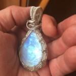 Hand holding a teardrop-shaped gemstone pendant with detailed wire wrapping