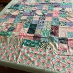 A colorful patchwork quilt with a floral border is spread out on a table.