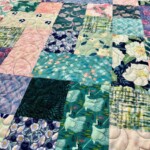 A colorful quilt with various patterned squares, including floral, geometric, and crane designs, is neatly stitched together.