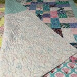 A colorful patchwork quilt with floral patterns is spread on a bed, showing detailed stitching and various fabric designs.